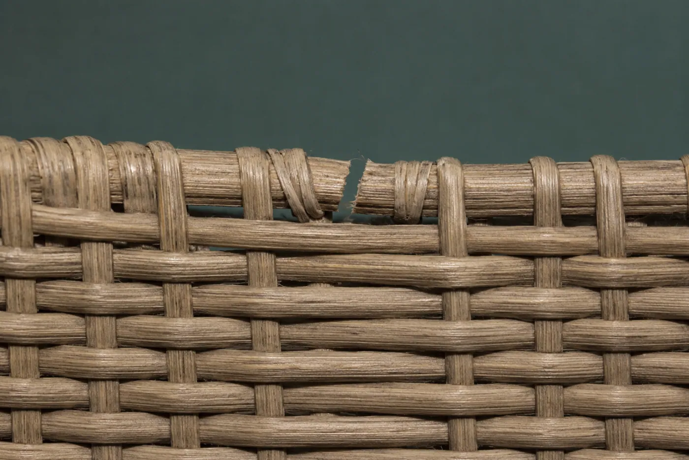 A broken strand in a woven rattan wall, the two cut ends spliced and tucked, not retouched.