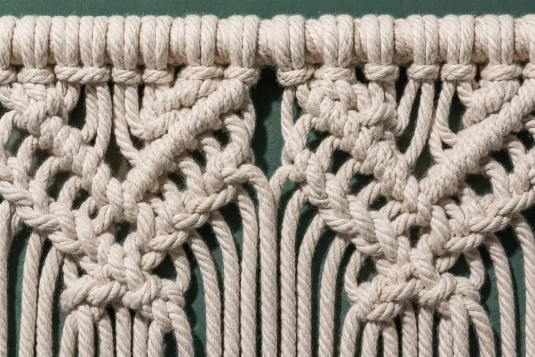 The weave and rim of ON-D-06 in close-up. Knotted downward from the rail in four sinnets, mirrored against its pair; the fringe is cut in two passes.